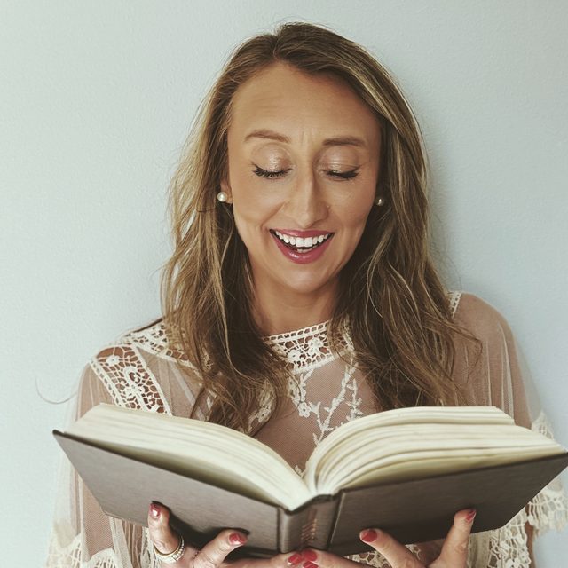Polaroid of Mar, smiling with her eyes on an open book, in a cream lace top.
